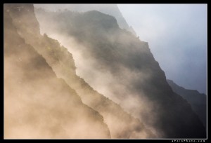 Heavy sea mist hugs the Na Pali coast as the setting sun illuminates it along the cliffs.