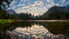 Sunrise in Yosemite with Half Dome, El Capitan, and rippling clouds in a perfect mirror reflection on the Merced River below.