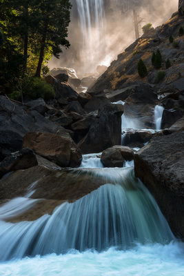 Beams of light through the mist of Vernal Fall in the background with flowing turquoise rapids in the foreground, Yosemite National Park, California