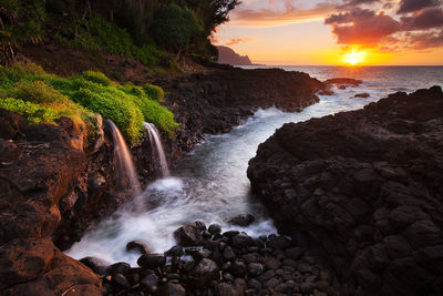 Sunset at Queens Bath shows flowing water, sea spray, Bali Hai mountain and golden-lit clouds from Princeville, Kauai, Hawaii.