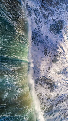 Breaking wave photographed from above shows sunlight filtering through pine trees onto water at Lumahai Beach, Kauai, Hawaii.