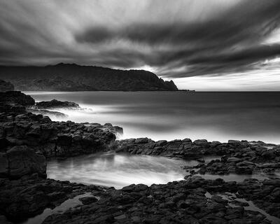 Rocky tidal pool of Queens Bath in Princeville, Kaua’i beneath stormy coastline.