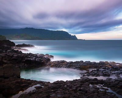Long exposure creates smooth flowing water over dark volcanic rocks at Queens Bath tidal pools, Princeville, Kauai, Hawaii.