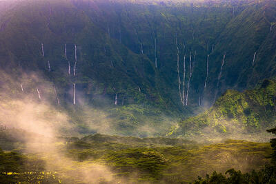 Fine art photograph of Mt. Waialeale after heavy rains showcasing numerous waterfalls streaming down the crater with mist in the foreground at Wailua, Kauai